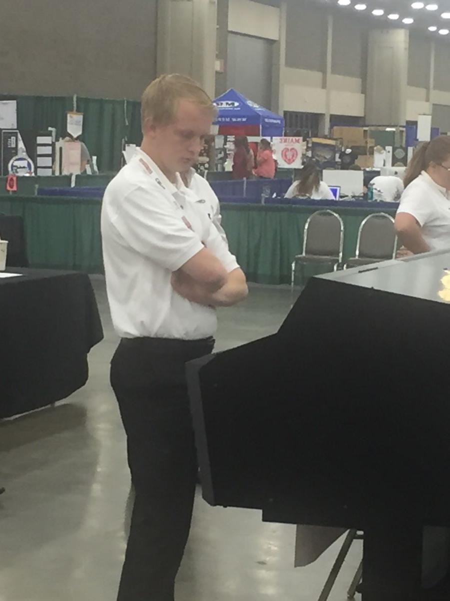 A young Caucasian college student in a white polo shirt and black dress pants, Hunter Steed, stares down at a graphics display during the competition.